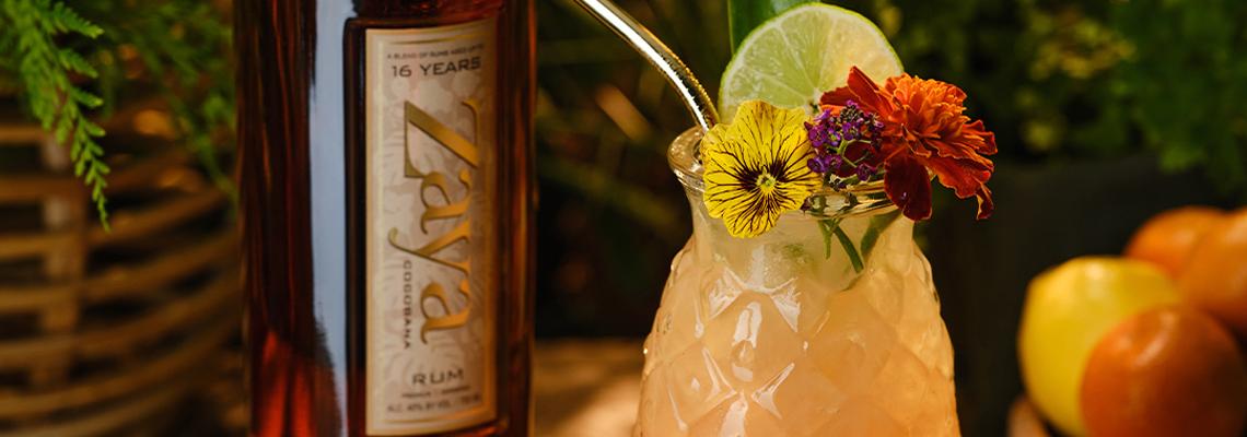 A bottle of Zaya Cocobana next to a delicious looking tropical cocktail in a pineapple glass with flower and lime wheel garnish.