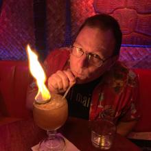 Photo of Kevin Crossman sipping a flaming cocktail at Hale Pele